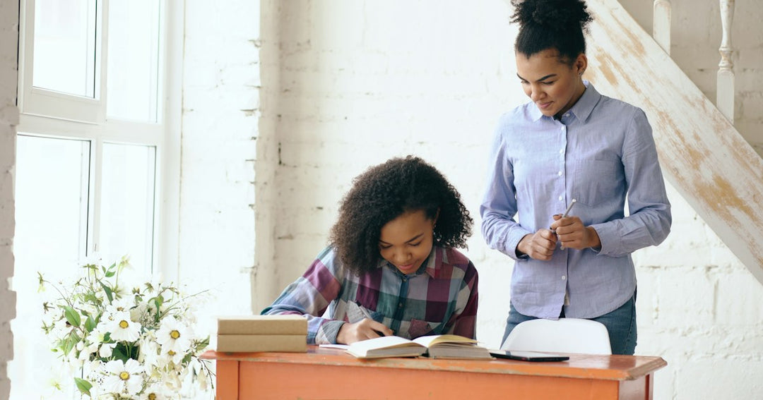 Une étudiante écrit ses réponses dans un cahier pendant que son enseignante relit son travail, comme lors d’un entraînement à la compréhension écrite du DELF B2